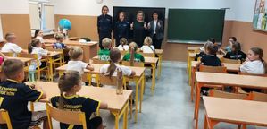 Cztery kobiety stoją na środku sali, w której przed nimi w ławkach siedzą uczniowie.