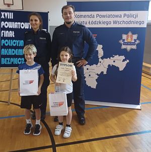 Policjanci stoją z dziećmi na sali sportowej.