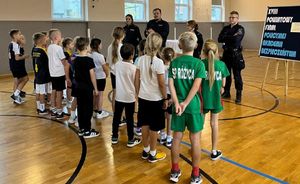 Policjanci stoją z dziećmi na sali sportowej.