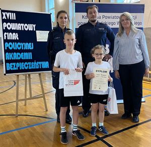 Policjanci stoją z dziećmi na sali sportowej.