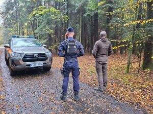 Policjant i strażnik leśny stoją obok samochodu na terenie lasu.
