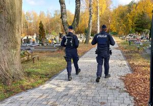 Policjanci idą cmentarną alejką.