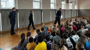 Policjanci stoją na środku sali, przed nimi siedzi duża grupa uczniów.