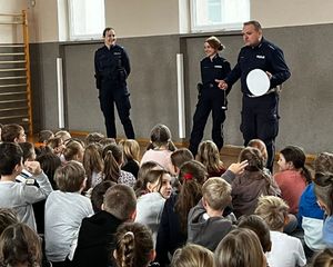 Policjanci stoją na środku sali, przed nimi siedzi duża grupa uczniów.
