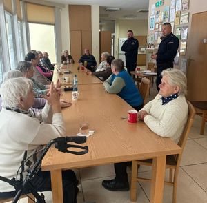 Policjanci rozmawiają z seniorami którzy siedzą przy stole.