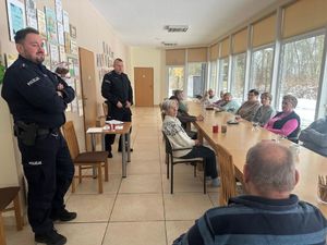 Policjanci rozmawiają z seniorami którzy siedzą przy stole.