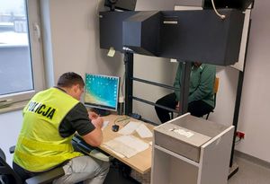 Policjant siedzi przed monitorem komputera, przed nim siedzi zatrzymana kobieta.