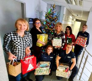 Policjanci i pracownicy stoją przy choince z prezentami dla podopiecznych.