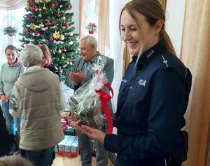 Policjanci stoją na środku salonu w domu pomocy społecznej wraz z personelem i podopiecznymi.