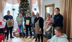 Policjanci stoją na środku salonu w domu pomocy społecznej wraz z personelem i podopiecznymi.