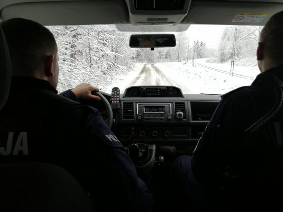 Dwóch policjantów jedzie radiowozem po ośnieżonej drodze.
