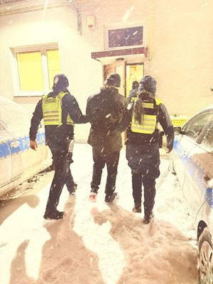 Policjanci prowadzą zatrzymanego mężczyznę.