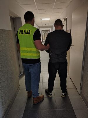 Policjant prowadzi zatrzymanego mężczyznę.