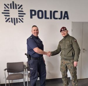 Policjant i funkcjonariusze wojska stoją ustawieni do zdjęcia, nad nimi jest napis Policja.