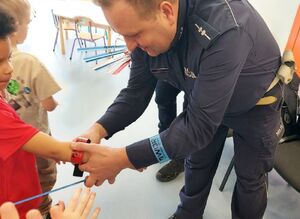 Policjant przypina opaskę odblaskową na rączkę dziecka.