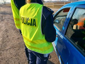 Policjanci stoją przy niebieskim samochodzie.