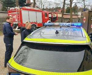 Policjanci stoją przy radiowozie i promują zawód policjanta.