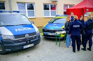 Policjanci stoją przy radiowozie i promują zawód policjanta.