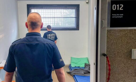 Policjant stoi przy zatrzymanym mężczyźnie.