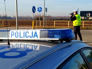 Policjant stoi przy drodze i mierzy prędkość.
