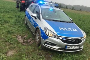 Policyjny radiowóz stoi na polu przed traktorem.