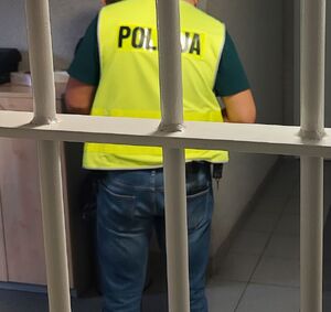 Policjant zapina kajdanki na ręce z tyłu mężczyzny za okratowanymi drzwiami.