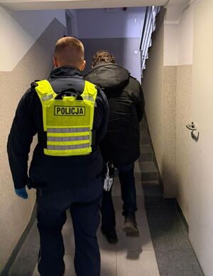Policjant prowadzi zatrzymanego mężczyznę.