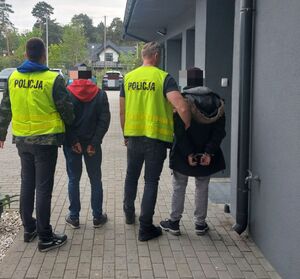 Dwóch policjantów prowadzi dwóch zatrzymanych mężczyzn.
