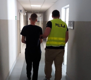 Policjant prowadzi zatrzymanego mężczyznę.