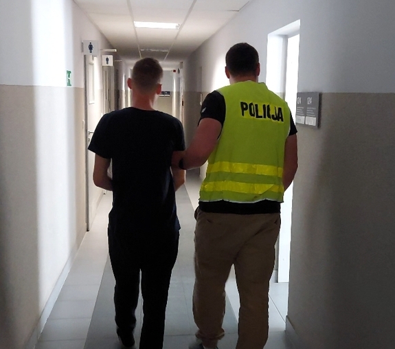 Policjant prowadzi zatrzymanego mężczyznę.