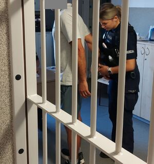 Policjantka zapina kajdanki zatrzymanemu.