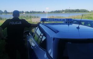 Policjant przy radiowozie patrzy w stronę wody.