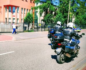 Policjanci na motocyklach jeżdżą obok szkoły.