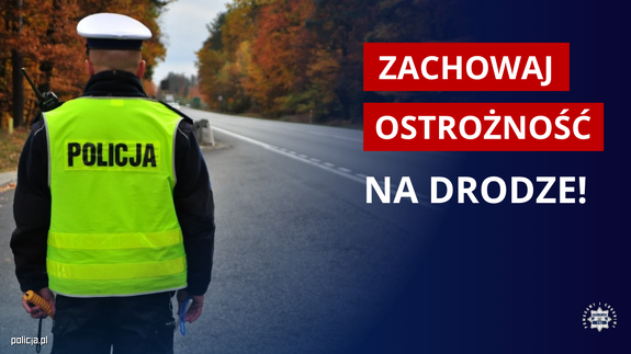 Policjant stoi na drodze napis obok Zachowaj ostrożność na drodze.